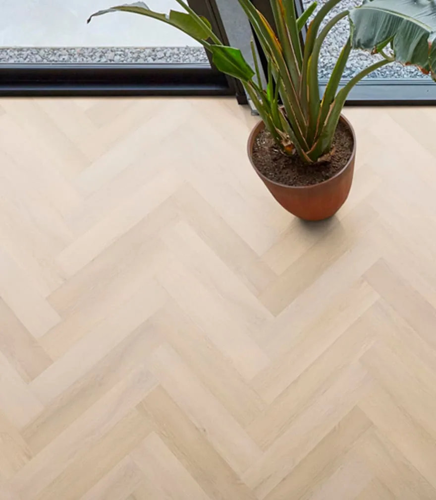Detail van een lichte PVC-visgraatvloer met een kamerplant bij het raam